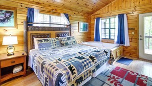 A wooden cabin bedroom with a large bed, a nightstand, a window with curtains, and a door. - Tennessee Cabin w/ Balcony, Hot Tub & Pool Access! (Sevierville)