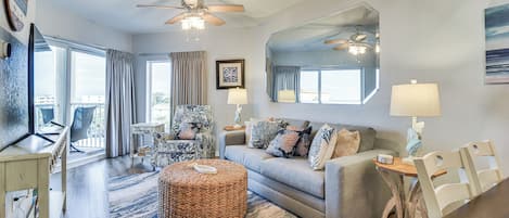 A spacious living room with a sofa, ottoman, and chairs, a dining table, and a ceiling fan.