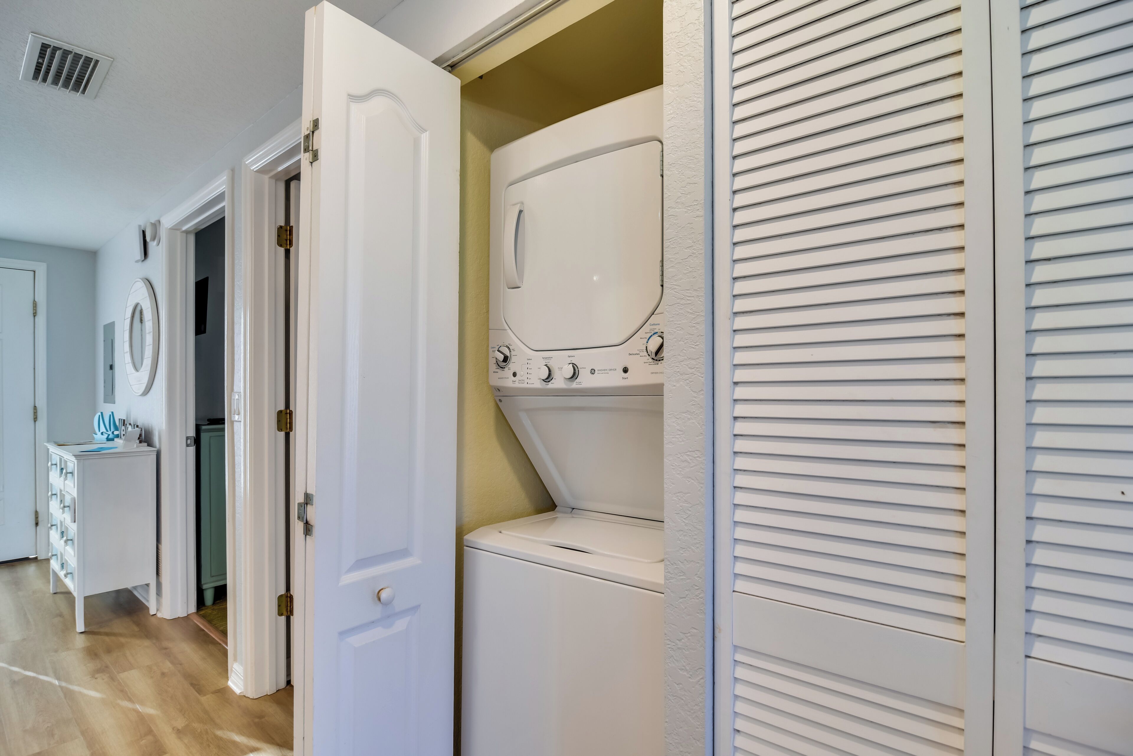 A laundry room with a front-loading washer and dryer, a white door, and a wooden floor.