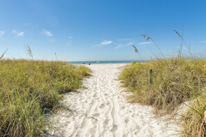 Ein sandiger Pfad führt zu einem Strand, begleitet von hohem Gras an beiden Seiten.