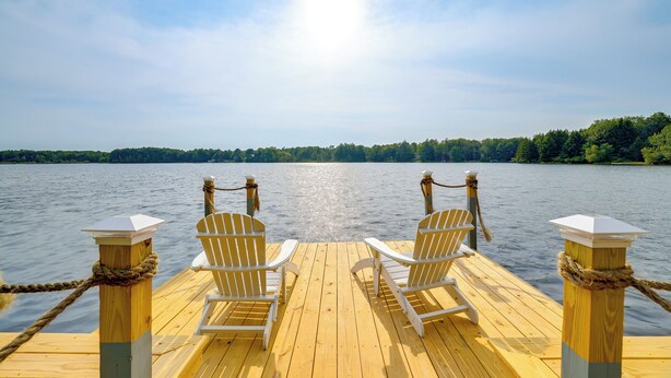 Un muelle de madera con dos sillas Adirondack blancas mirando a un lago tranquilo.