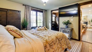 Un dormitorio bien iluminado con una cama grande, televisor, escritorio y baño visible a través de una puerta abierta.