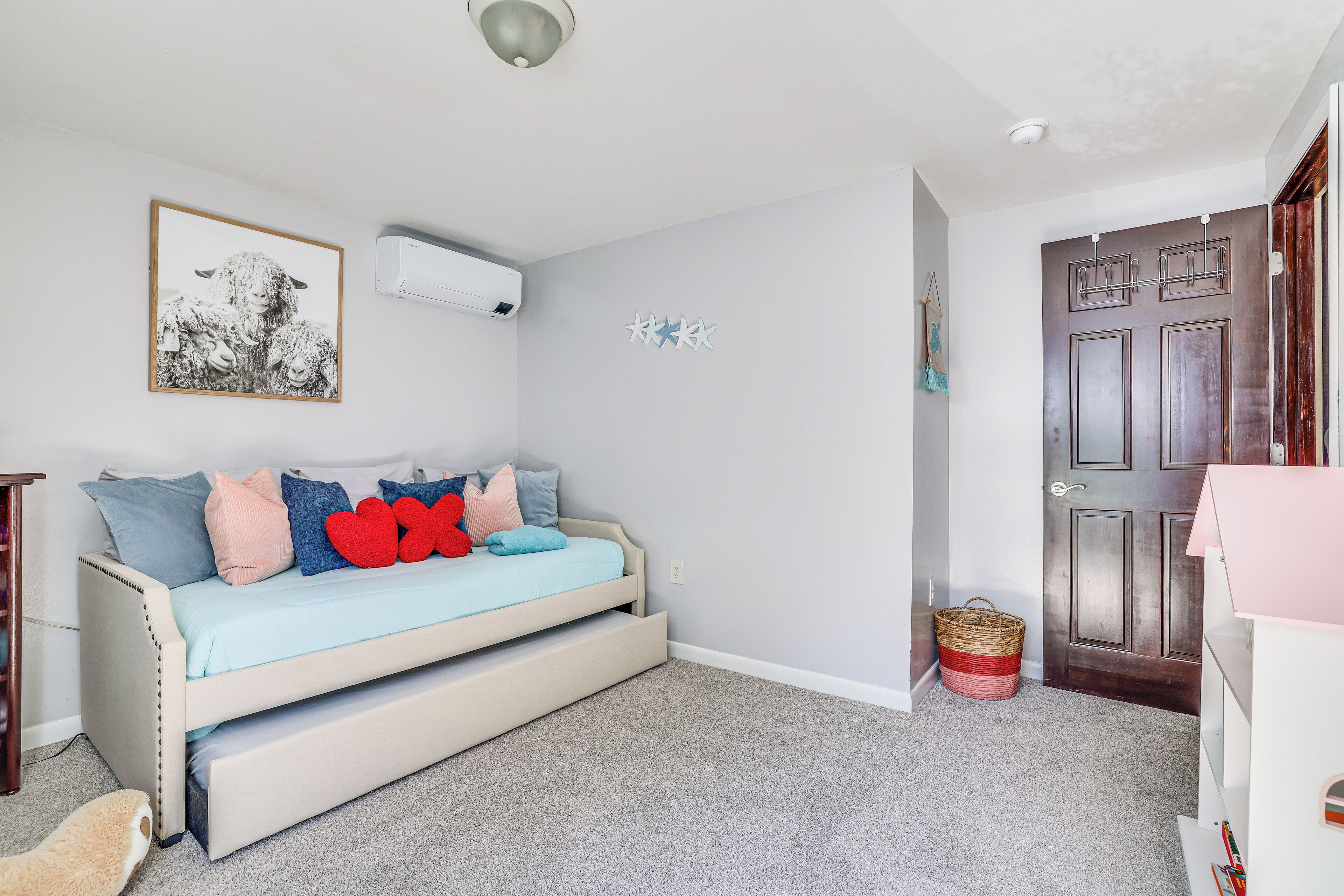 Une chambre avec un lit, un climatiseur fixé au mur, une porte et un petit panier.