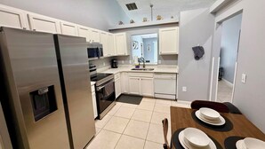 A modern kitchen with white cabinets, stainless steel appliances, and a dining area with a wooden table and chairs. - Grand Luxury Pines 3BR Pool Home near Disney (Davenport)