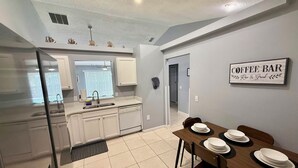 A modern kitchen with white cabinets, a dining area with a wooden table set for four, and a sign reading "Coffee Bar". - Grand Luxury Pines 3BR Pool Home near Disney (Davenport)