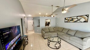 A living room with a sectional sofa, a glass coffee table, a flat-screen TV, and a ceiling fan. - Grand Luxury Pines 3BR Pool Home near Disney (Davenport)