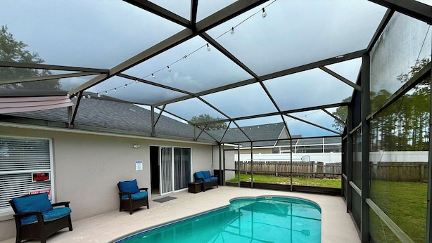 A covered outdoor swimming pool with a patio area, chairs, and a view of the backyard. - Grand Luxury Pines 3BR Pool Home near Disney (Davenport)