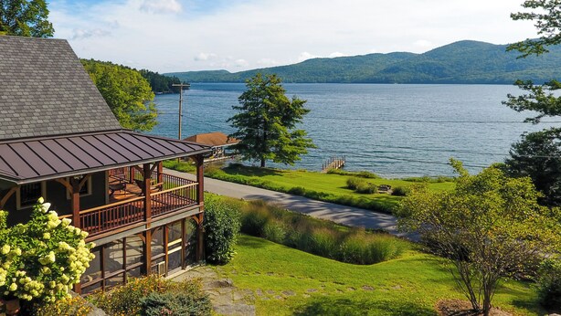 A lakeside cabin with a deck, a stone pathway, and a view of the lake and mountains. - Serene Silver Bay Home on Lake George w/ Boat Slip (Silver Bay)