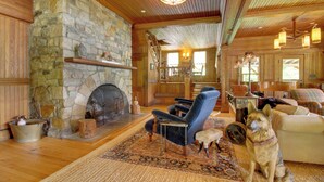 A cozy living room with a stone fireplace, wooden floors, a blue armchair, a dog, and a couch. - Serene Silver Bay Home on Lake George w/ Boat Slip (Silver Bay)