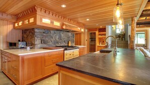 A spacious kitchen with wooden cabinets, a stone accent wall, and a large island with a sink. - Serene Silver Bay Home on Lake George w/ Boat Slip (Silver Bay)