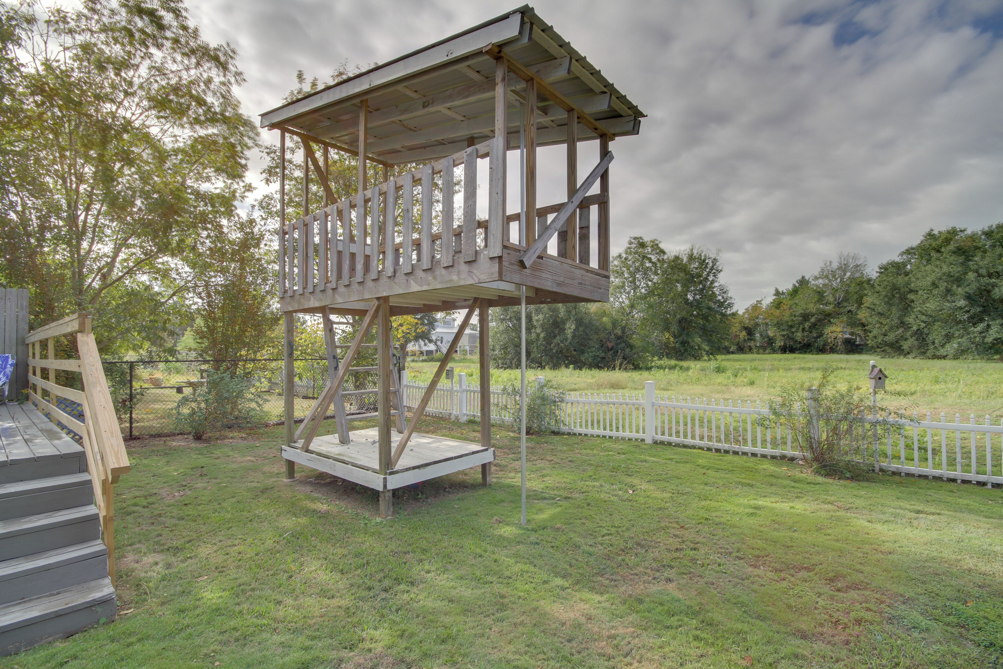 Une tour d’observation en bois, dotée d’une plateforme et d’un escalier, entourée d’une clôture en bois peinte en blanc et de verdure.