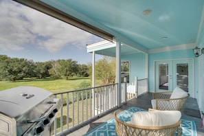 A covered porch with a grill, wicker chairs, and a view of a grassy yard.