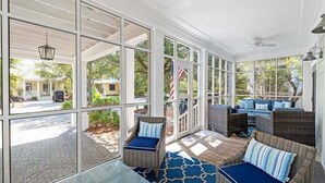 A covered patio with wicker furniture, large windows, and a glass table. - WaterColor! Steps to Seaside, WC Tennis! LSV/Golf Cart & 2 Bikes Included! Secluded but Central! (Santa Rosa Beach)