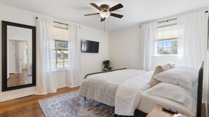 Ein Schlafzimmer mit Bett, Deckenventilator, Fernseher und großem Spiegel.