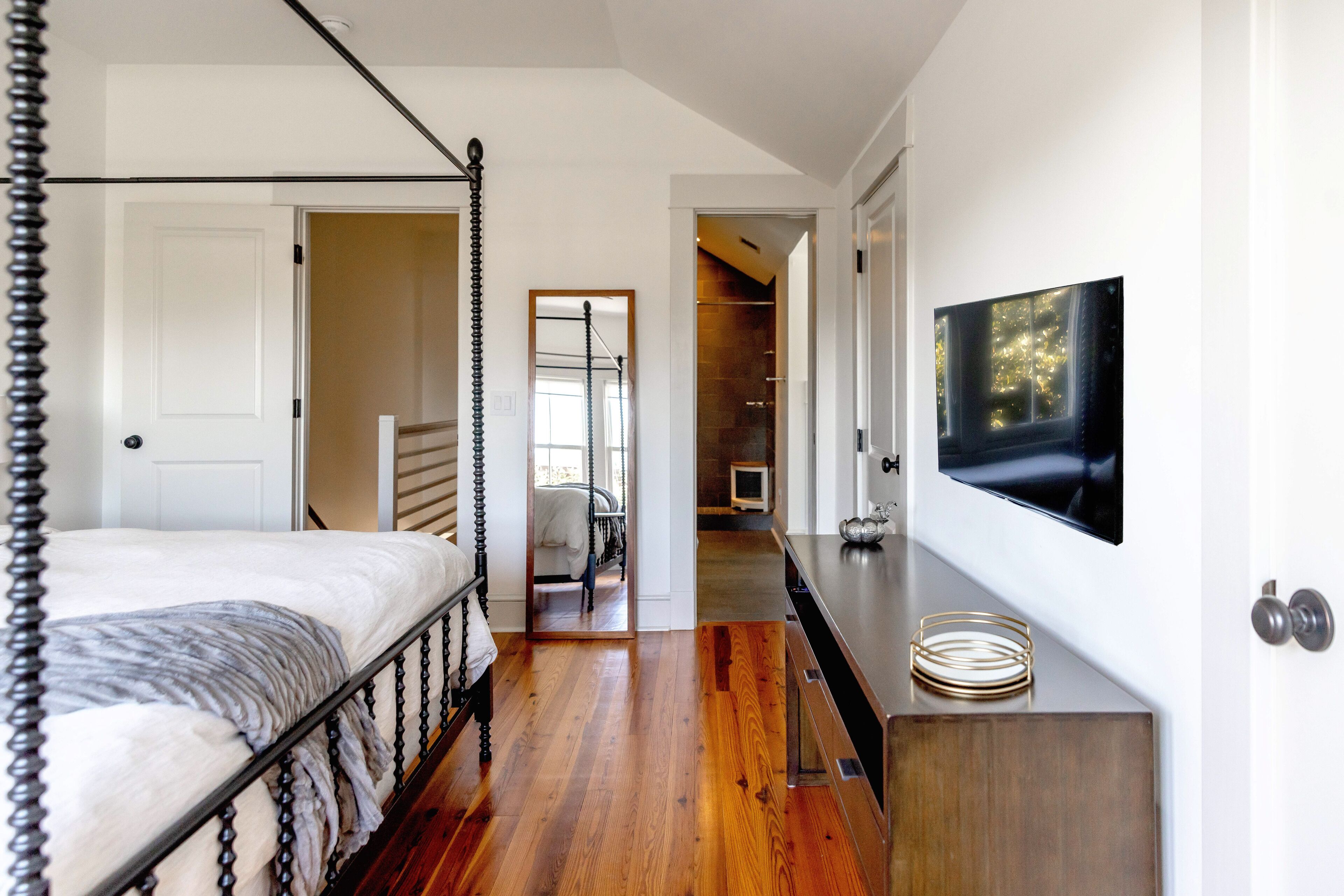 Une chambre à coucher avec un lit à baldaquin, un téléviseur fixé au mur et un plancher en bois.