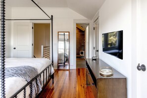 A bedroom with a four-poster bed, a television mounted on the wall, and a wooden floor. - 2BR Townhome Nestled on Historic Crawford Square (Savannah)