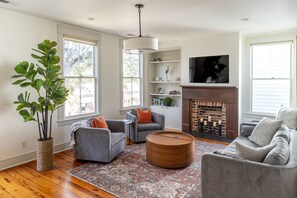 A living room with a fireplace, two grey sofas, a coffee table, and a large plant. - 2BR Townhome Nestled on Historic Crawford Square (Savannah)