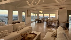 A spacious living area with a high ceiling, large windows offering ocean views, and a modern dining area. - Oceanfront 10 bdrm w/Pool/Elevator on The Point. Best Views on the Island! (Emerald Isle)