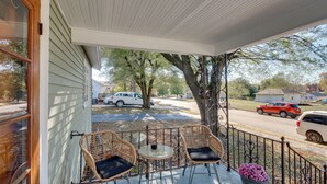 A covered porch with wicker chairs and a small table, overlooking a street with parked cars and houses. - Missouri Escape w/ Furnished Patio, Near Downtown! (Nevada)