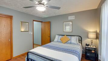 A bedroom with a bed, a ceiling fan, a nightstand with a lamp, and a mirror on the wall.