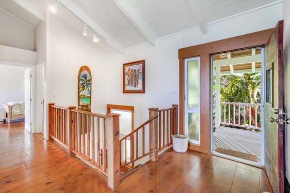 Una escalera de madera con barandilla blanca que lleva a un balcón con vista a zonas verdes.
