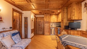 Una stanza accogliente con soffitto e pareti in legno, un divano con cuscini decorati, un tavolo da pranzo con un tappeto e un angolo cottura con mobili in legno e un televisore.