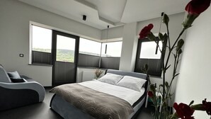 Une chambre à coucher moderne avec un grand lit, un canapé et une vue sur l’extérieur par les fenêtres.