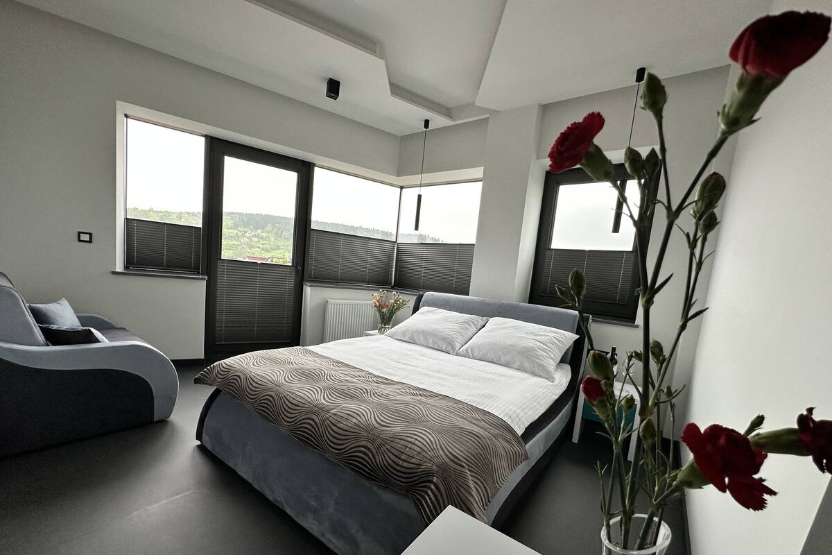 Une chambre à coucher moderne avec un grand lit, un canapé et une vue sur l’extérieur par les fenêtres.