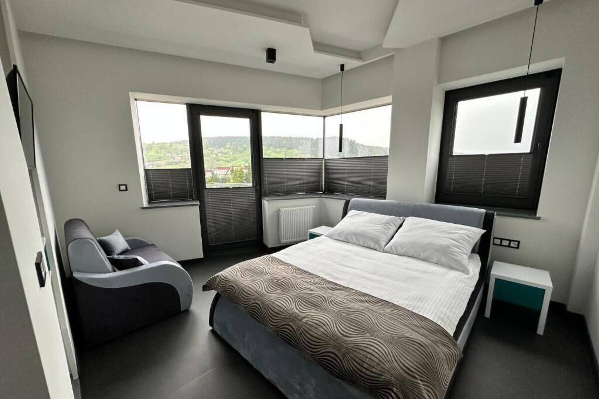 Une chambre à coucher moderne, dotée d’un grand lit, d’un canapé et offrant une vue sur l’extérieur grâce à de grandes fenêtres.