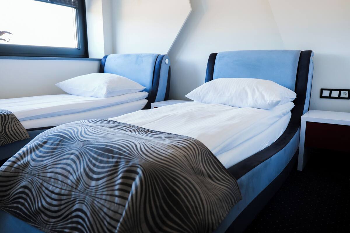 Une chambre d’hôtel avec deux lits simples, chacun doté d’une tête de lit, d’une fenêtre et d’une table de chevet.