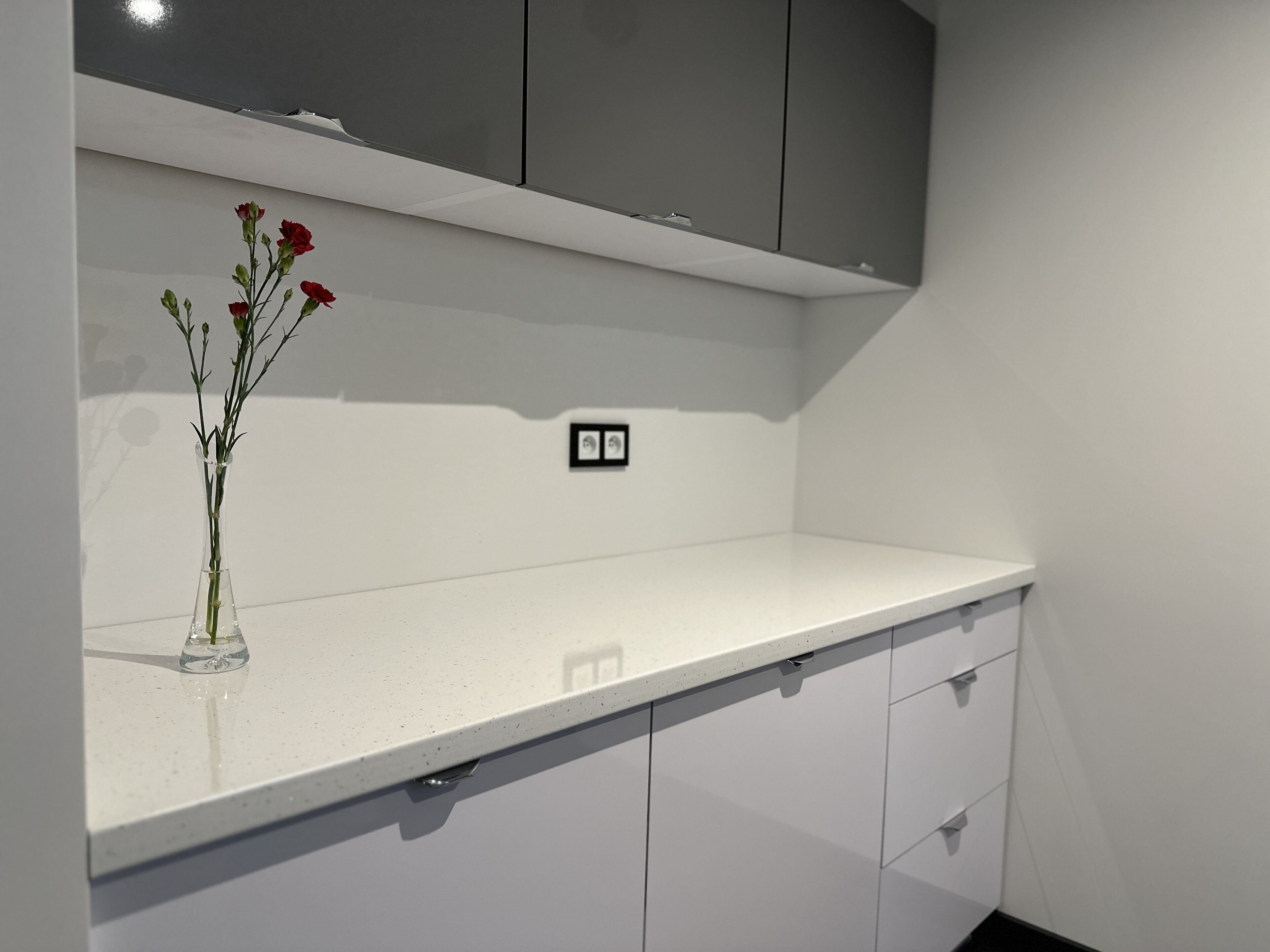 A kitchen with white cabinets, a white countertop, and a vase with flowers.