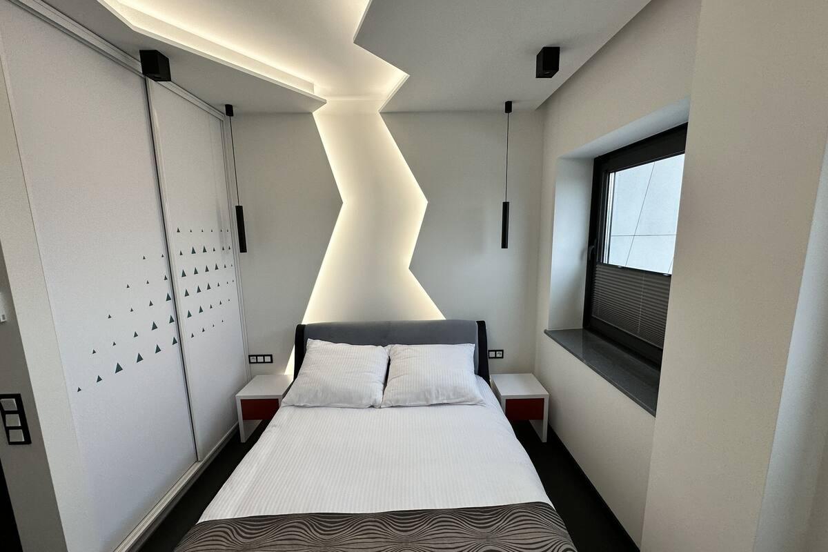 Une chambre d’hôtel moderne équipée d’un lit, de tables de chevet, d’une fenêtre et d’un plafond au design original.