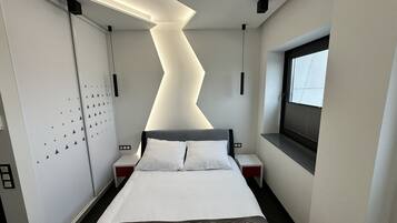 Una habitación de hotel moderna con cama, mesitas de noche, ventana y un diseño de techo original.