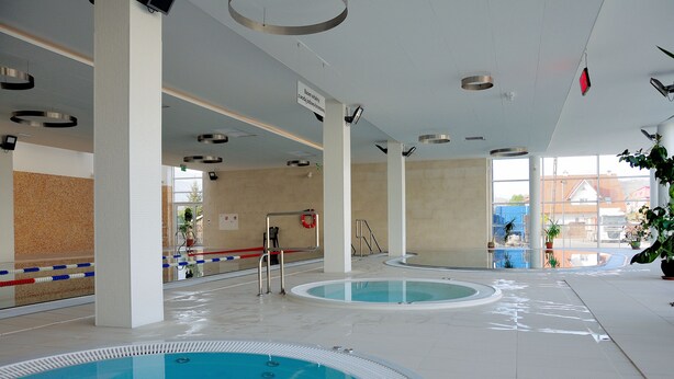 Une piscine intérieure dotée de plusieurs couloirs de nage, d’un poste de surveillance pour les sauveteurs et offrant une vue dégagée sur l’extérieur grâce à de grandes fenêtres.