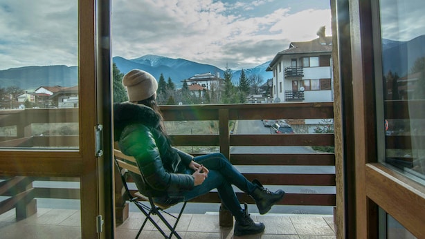 Une personne assise sur un balcon, avec vue sur les montagnes et les bâtiments.