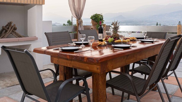 An outdoor dining area with a wooden table and chairs, a grill, and a view of the mountains. - Haritos Holidays Home (Pompia)
