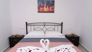 A neatly made bed with a heart-shaped towel arrangement, a painting of palm trees, and a pink bedspread. - Haritos Holidays Home (Pompia)