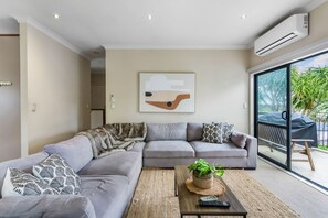 A modern living room with a grey sectional sofa, a coffee table with a plant, and a large window with a view of greenery.