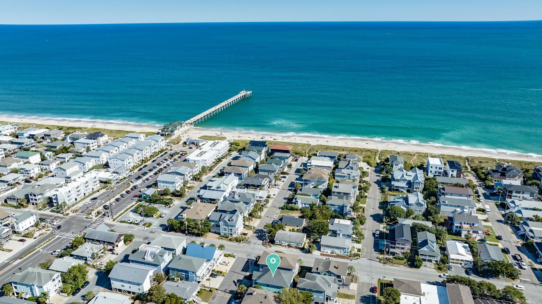 An aerial view of a coastal residential area with a pier extending into the ocean, surrounded by houses and a beach.