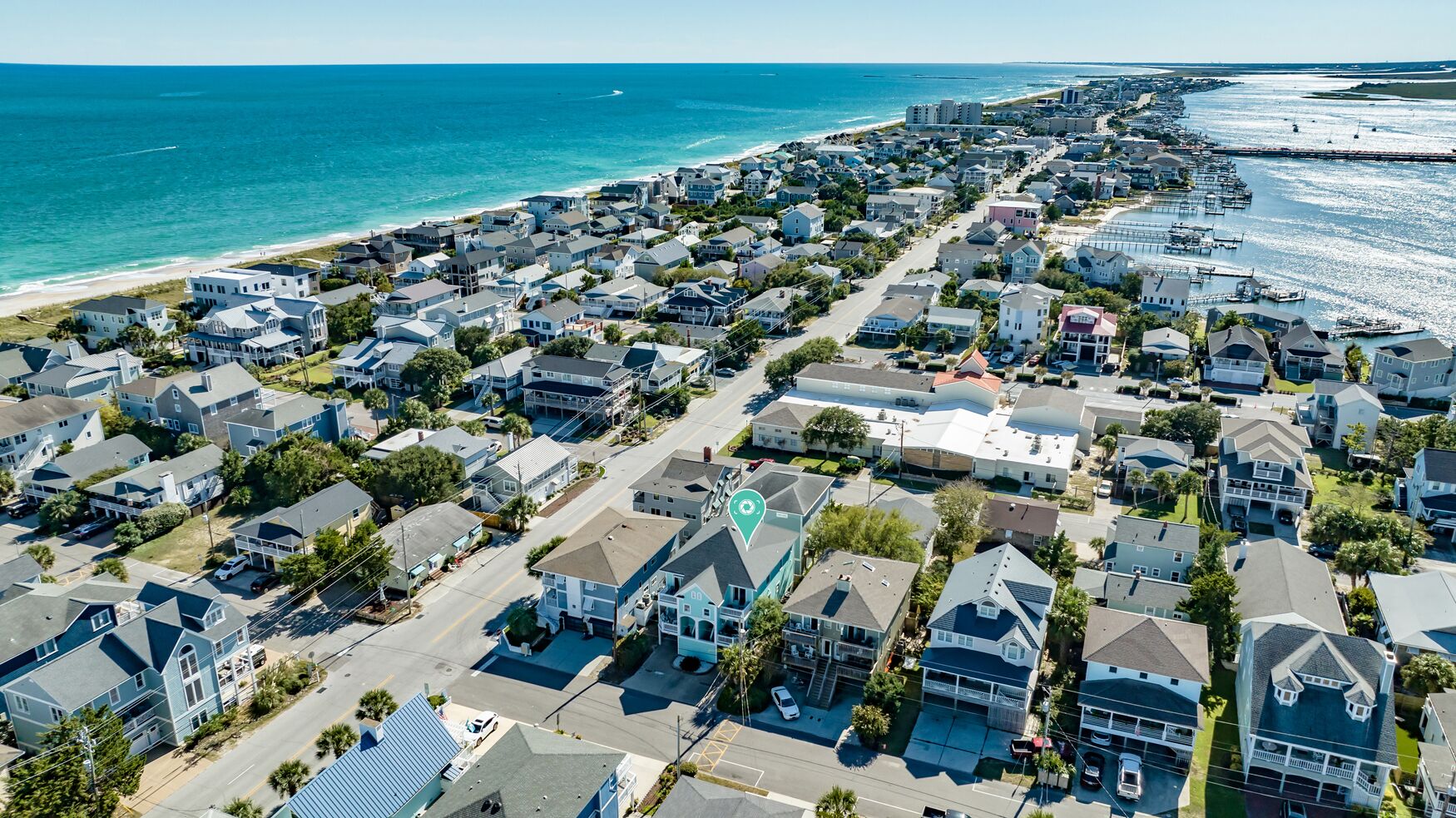 An aerial view of a coastal residential area with houses, a beach, and a marina.