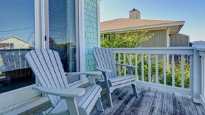 A wooden deck with two Adirondack chairs, a white railing, and a view of neighboring houses. - Beach Lovers' Paradise: Beach, Pier, and Dining Nearby! (Wrightsville Beach)
