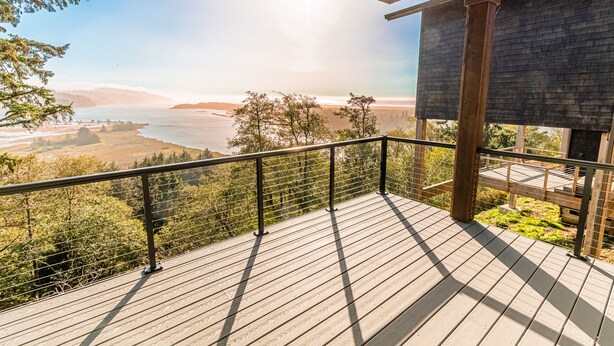 Une terrasse en bois avec une rambarde en métal, offrant une vue panoramique sur un paysage pittoresque comprenant un plan d’eau et des collines.