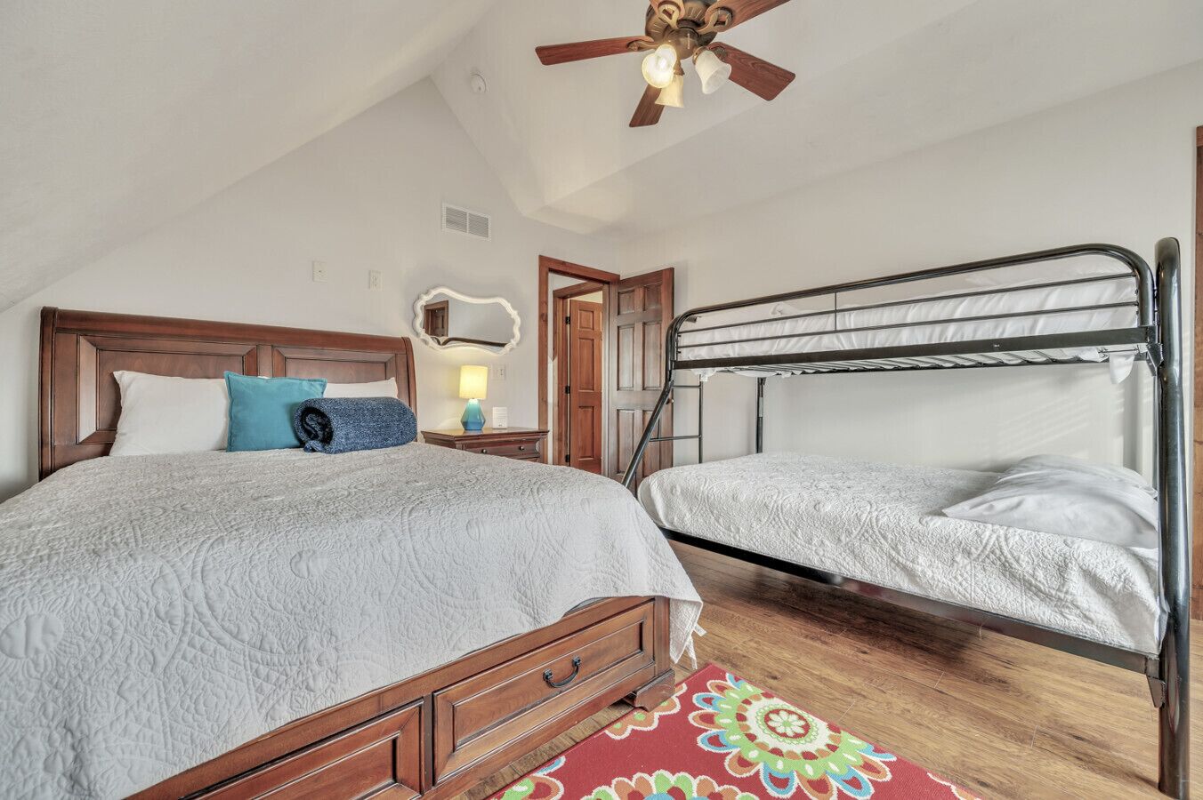 Un dormitorio con una cama de madera, una litera, un ventilador de techo y una alfombra estampada.