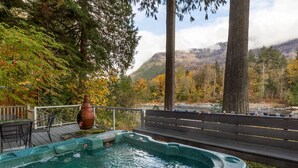 A hot tub on a wooden deck with a bench, surrounded by trees and a view of mountains. - Mountain Memories - river access, pet friendly w/ hot tub (Baring)
