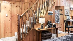 A wooden interior with a rustic staircase, a table with decorative items, and a chair. - Mountain Memories - river access, pet friendly w/ hot tub (Baring)