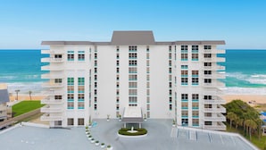 A multi-story hotel with a central courtyard, balconies, and a view of the beach and ocean.
