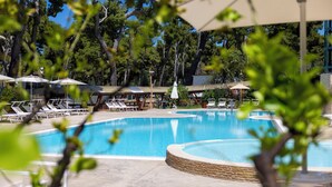 A swimming pool with lounge chairs and umbrellas, surrounded by trees and buildings. - Paglianza (Peschici)