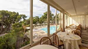 A dining area with large windows overlooking a pool and lush greenery. Tables are set with white tablecloths and numbered for reservations. - Paglianza (Peschici)