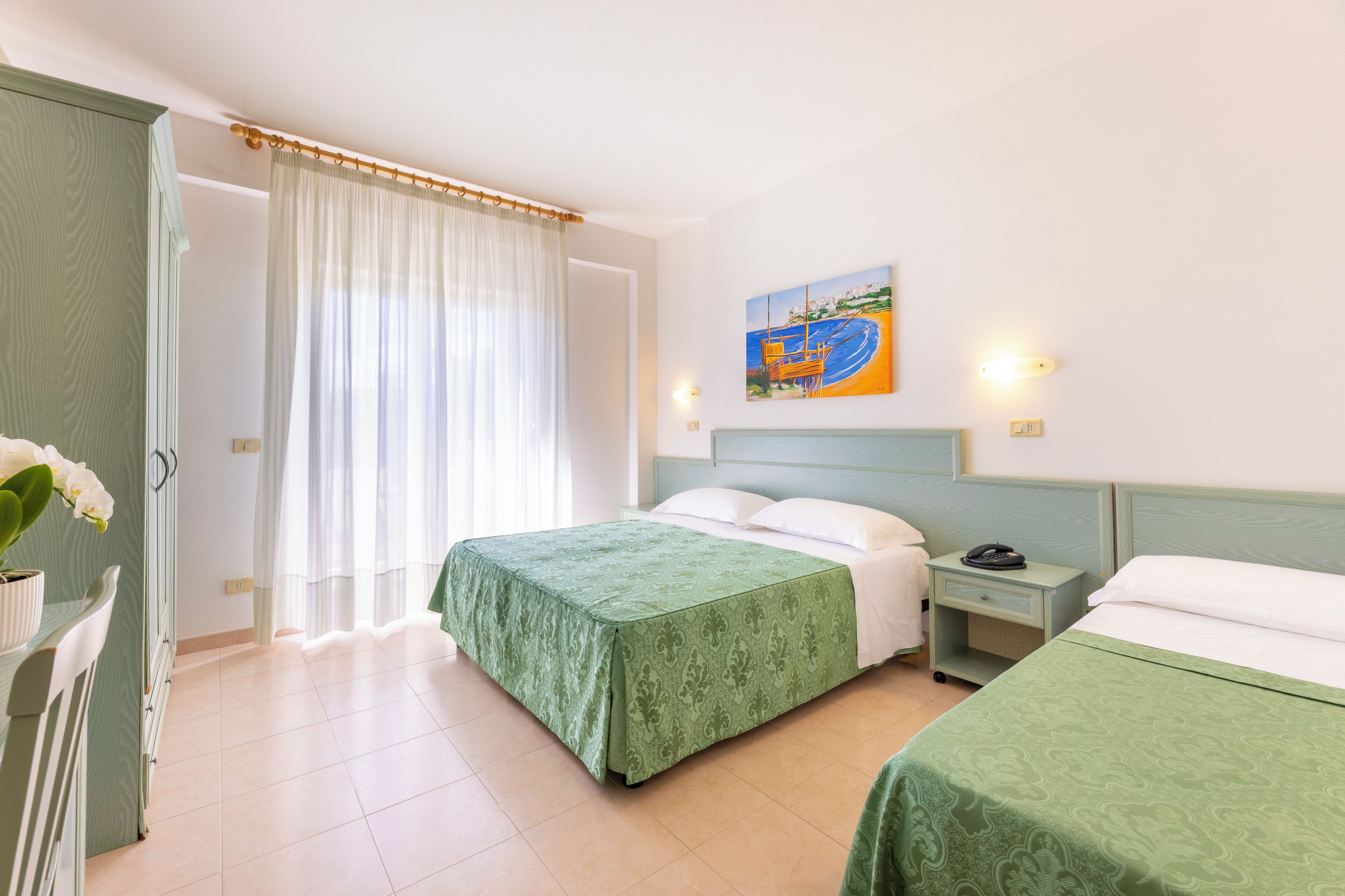A hotel room with a bed, a nightstand, a painting, and a window with curtains.