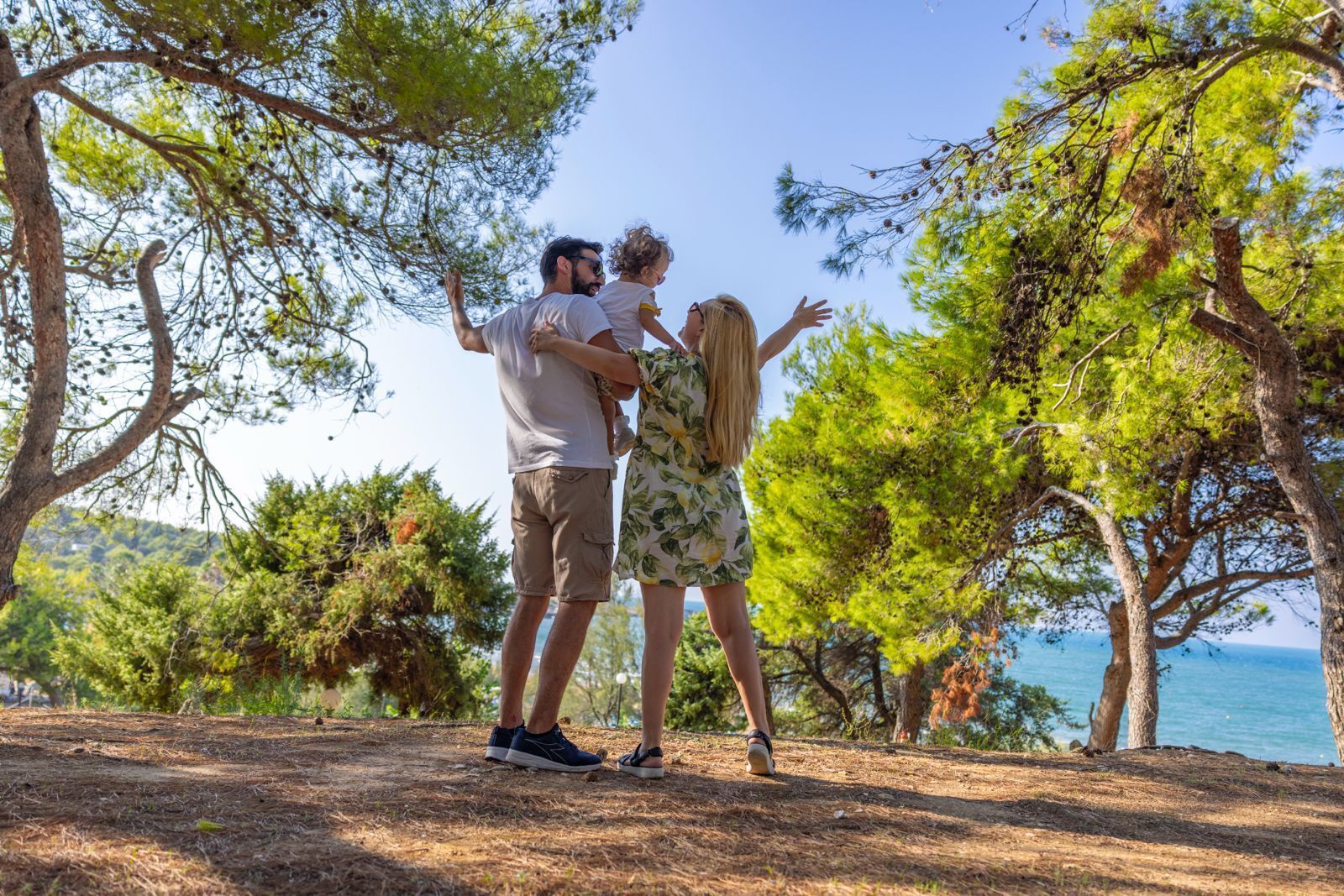 A family standing on a dirt path surrounded by trees with a view of the sea.
